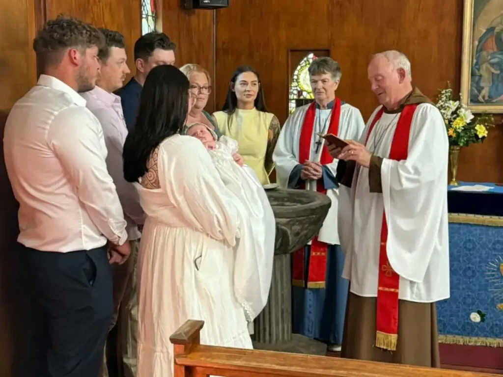 Family gathered around the stone font as an infant is presented for baptism at The Abbey Church